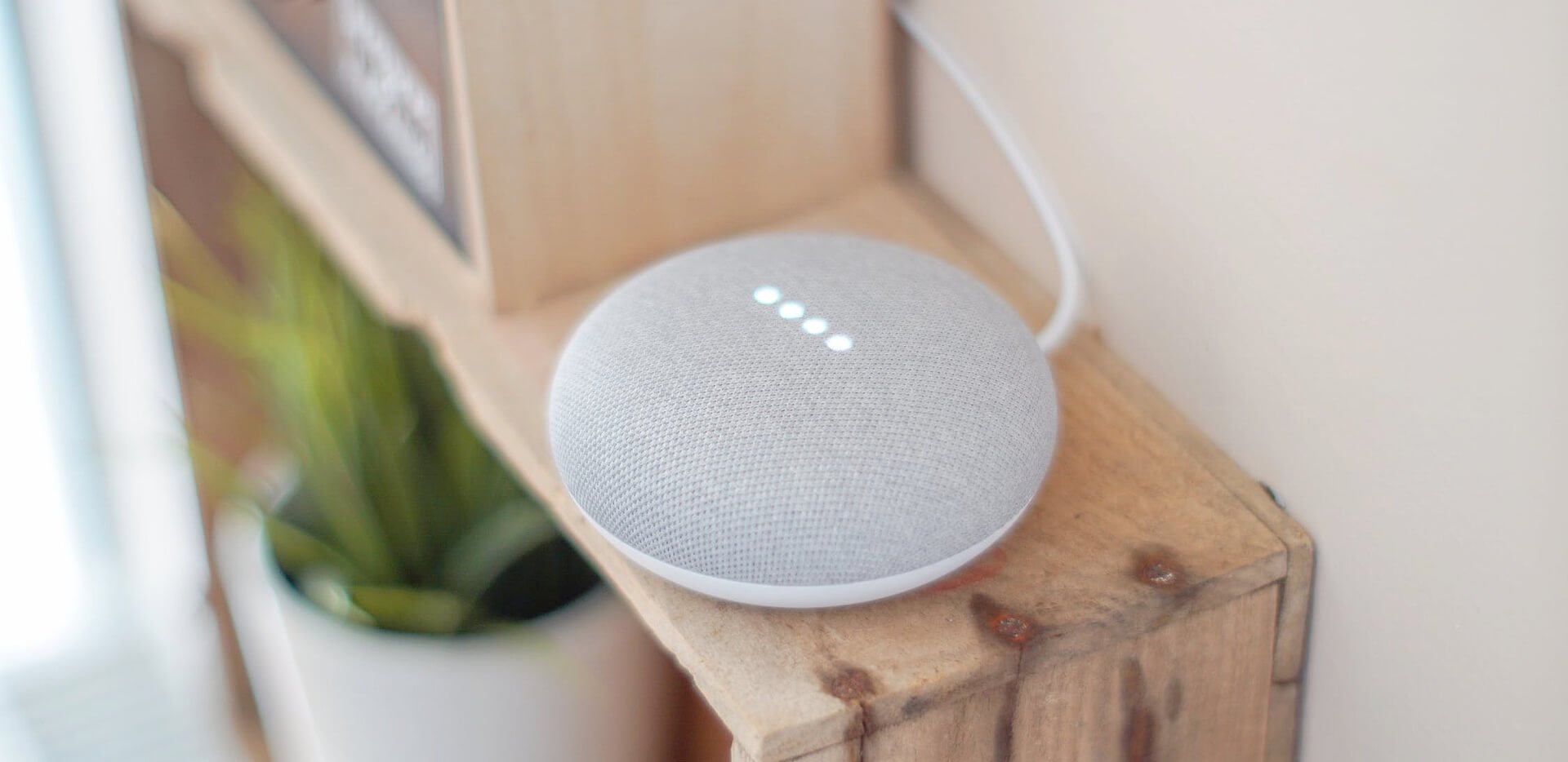 White Google Home Mini Placed On A Wooden Showcase