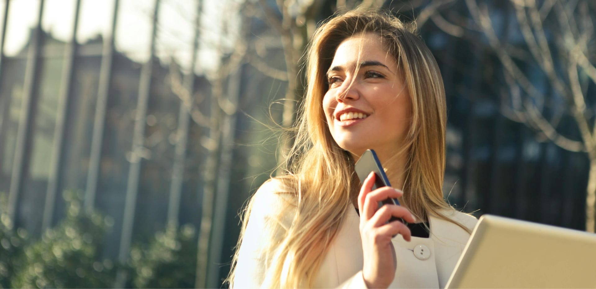 A confident businesswoman, holding a smartphone and tablet, smiles while looking forward, symbolizing successful digital transformation in B2B e-commerce, relevant to the Brosco International (BROMED) case study by Ceymox.